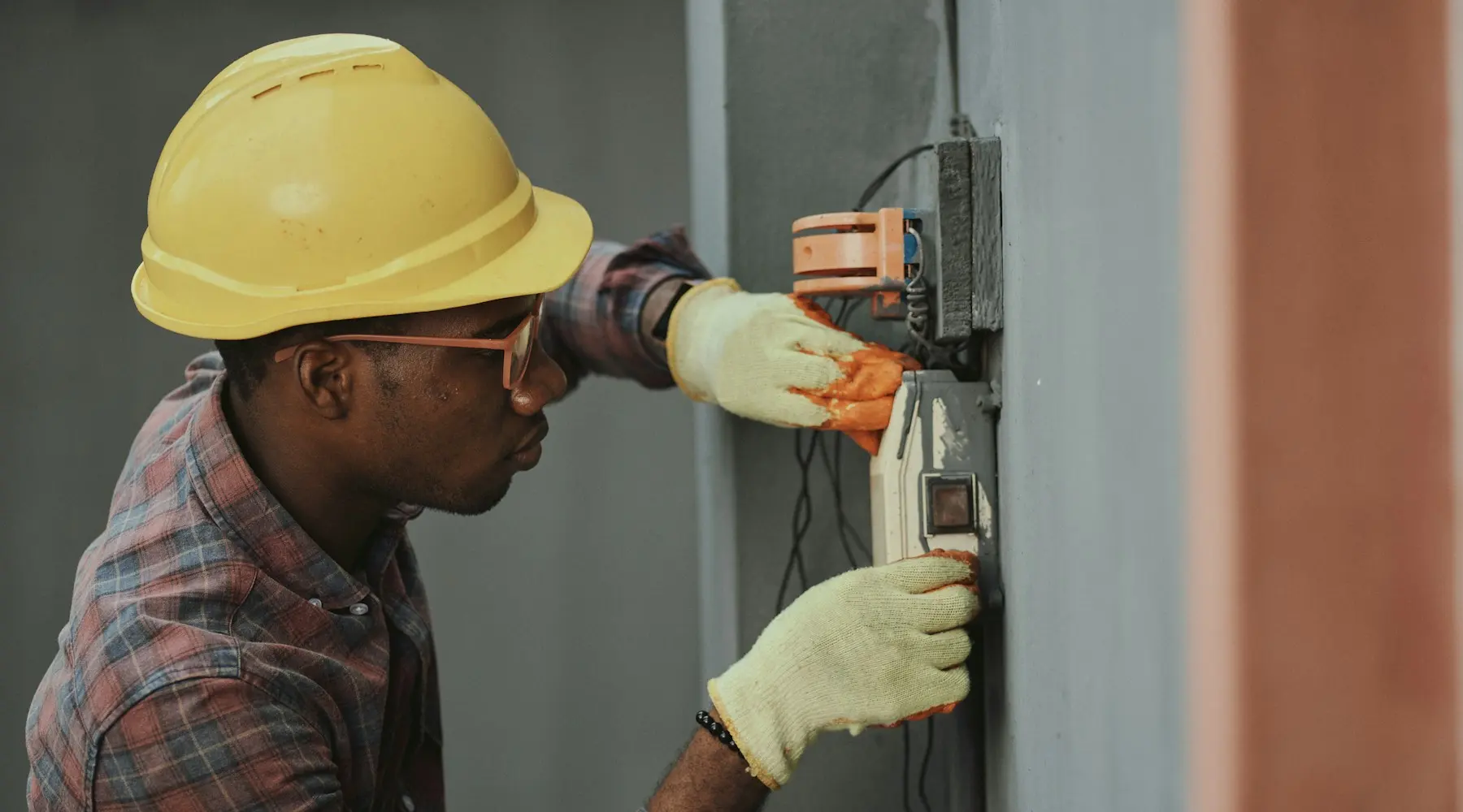 Electrician in a hard hat working at a wall panel